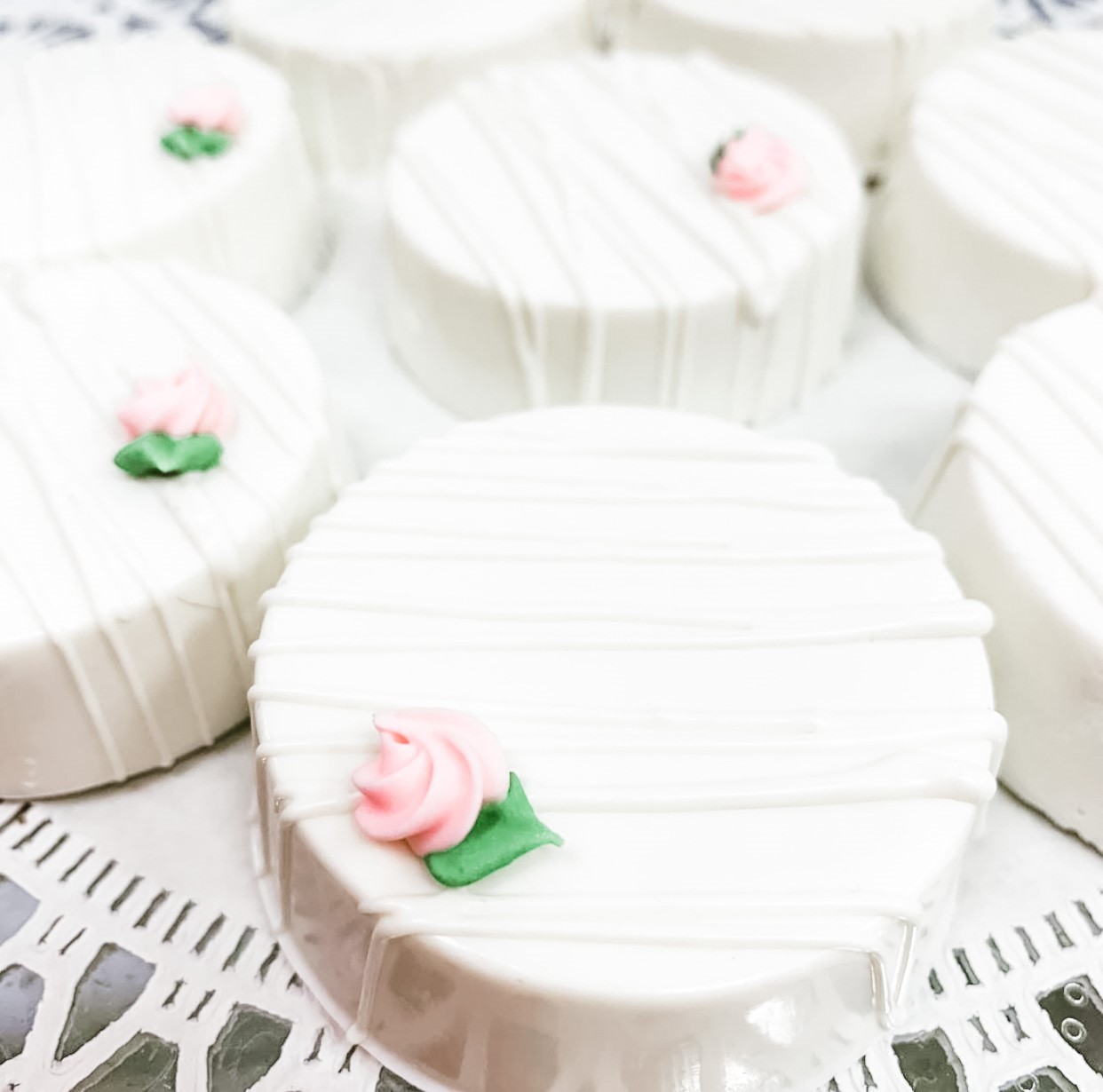 A platter of white chocolate covered Oreos with white chocolate drizzle pink sugar rose.