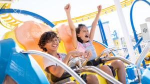 Two kids enjoy the Tidal Wave ride. One female rider holds arms up in excitement