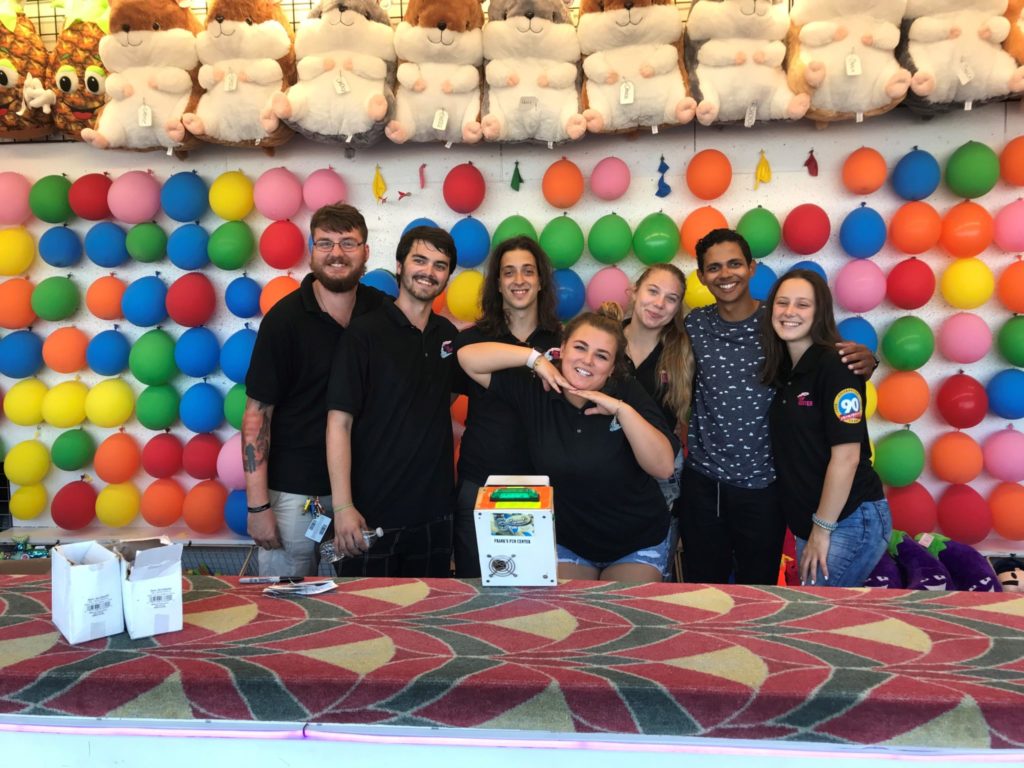A picture of seven employees behind the counter of one of the Balloon Popping Games at Jenkinson's.