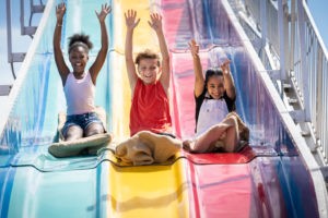 Three kids enjoy Fun Slide at Jenkinson's Boardwalk. Riders throw their hands in the air in excitement