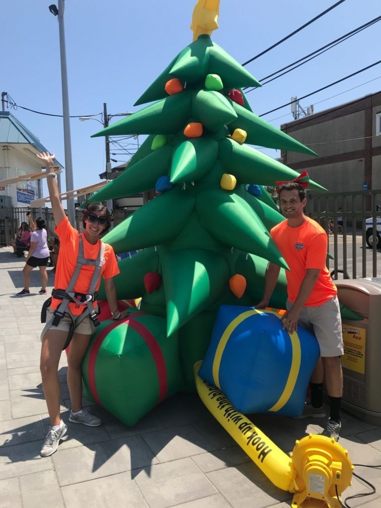 Two employees next to a Christmas tree inflatable for Christmas in July at Jenkinson's Boardwalk.