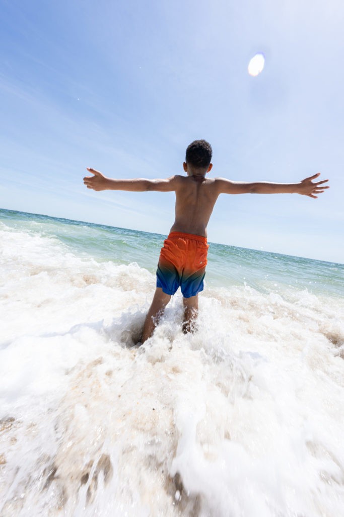 A male kid soaks up the sun with his hands out in the ocean at the beach located at Jenkinson's Boardwalk