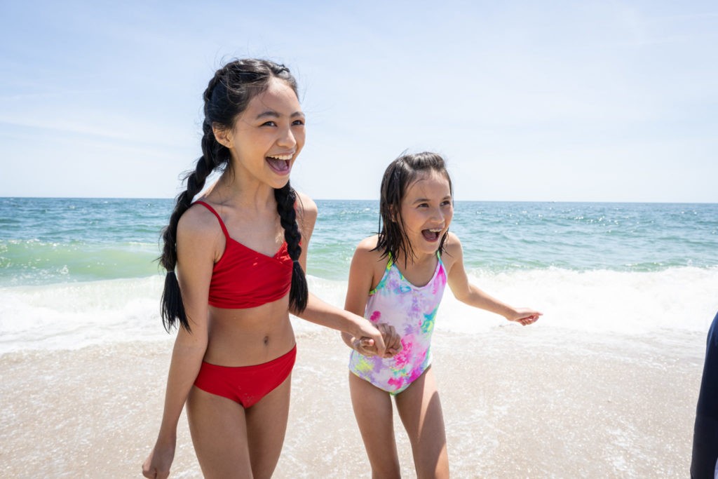 Two young females hold hands and smile at the beach located at Jenkinson's Boardwalk