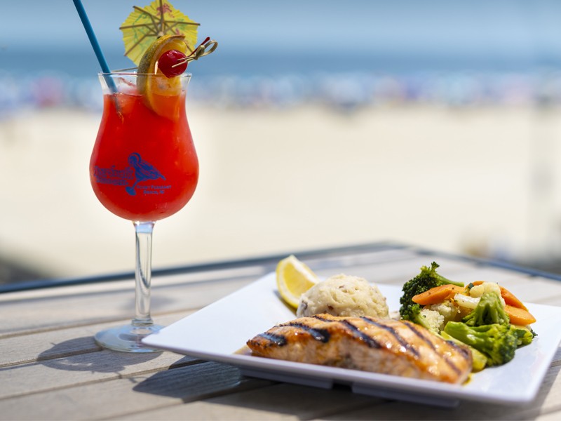 a red tropical drink with an entree overlooking the boardwalk and the beach at Jenkinson's Boardwalk