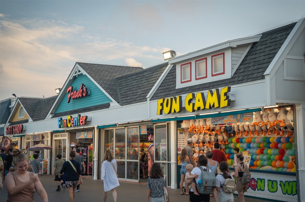 Individuals strolling by a shop with a sign advertising a "fun game".