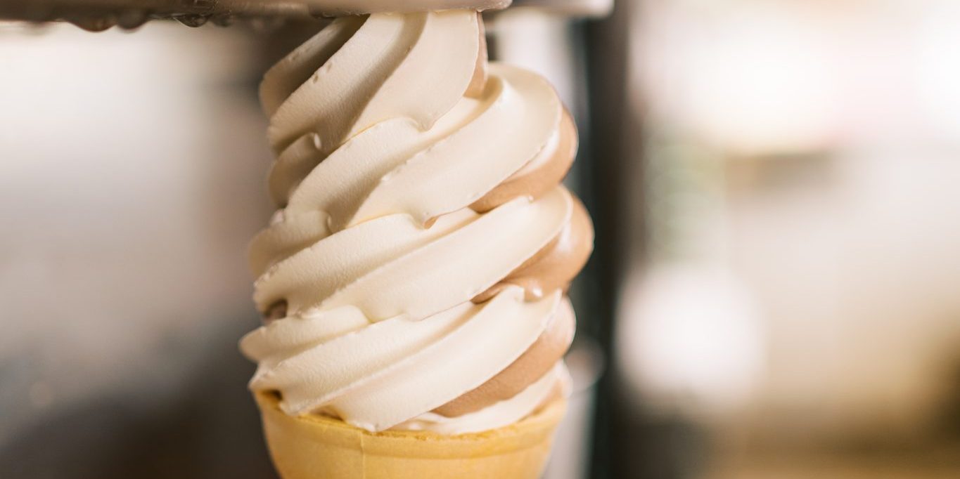 Hand holding a soft-serve ice cream cone being dispensed from a machine.