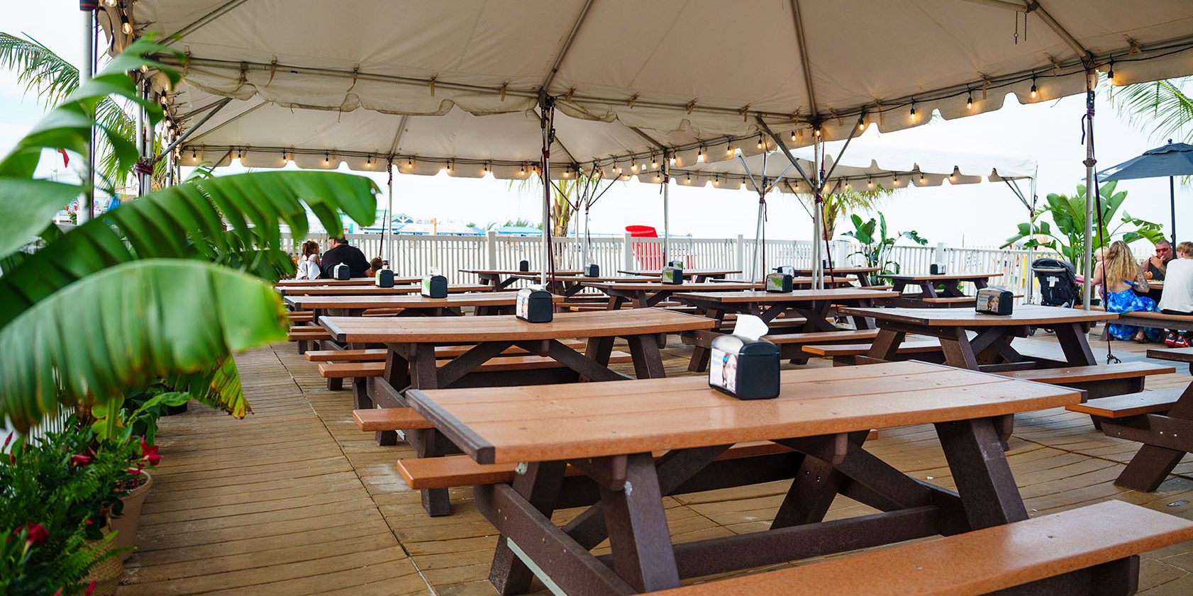 Covered outdoor seating area at Jenkinson's Boardwalk featuring rows of wooden picnic tables under a large white tent overlooking the beach.