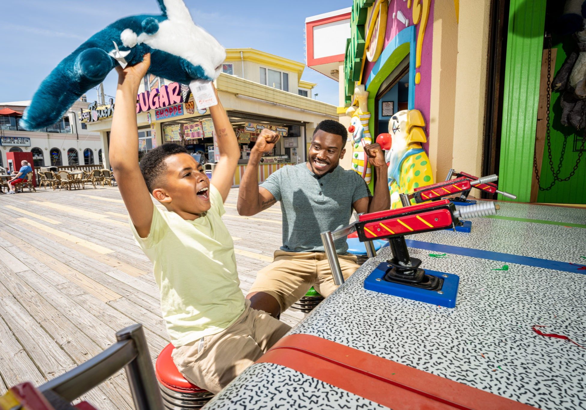 A father and son enjoy water gun game at Jenkinson's Boardwalk. Son holds up stuff shark toy after winning game