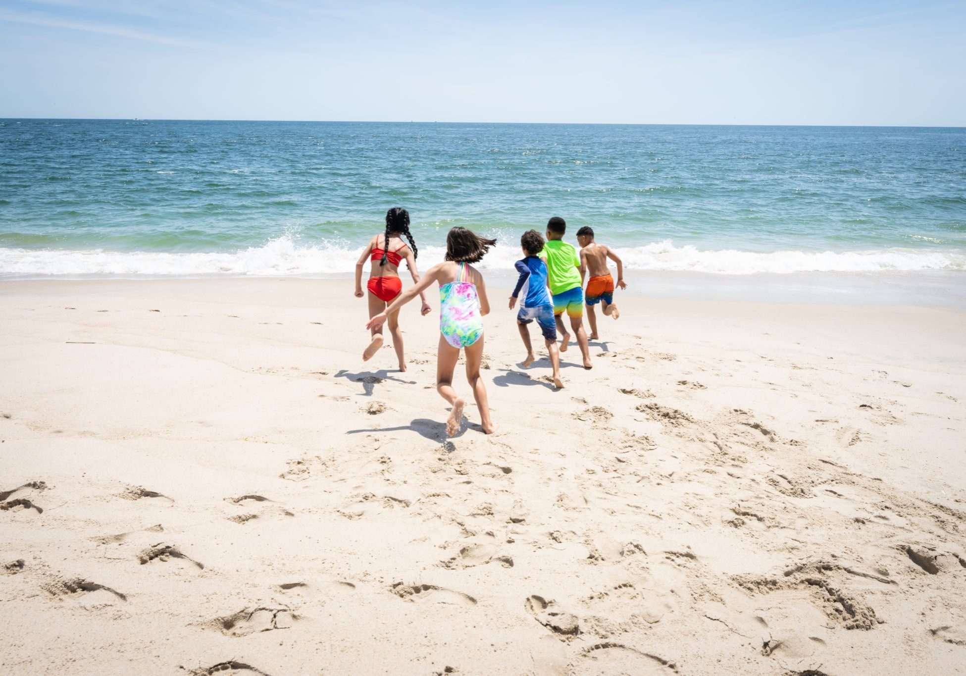 Five kids run toward the ocean in the sand at the beach located at Jenkinson's Boardwalk
