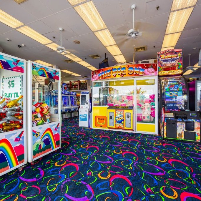 Bright indoor arcade with claw machines, prize games, and colorful carpet at Jenkinson’s Boardwalk.