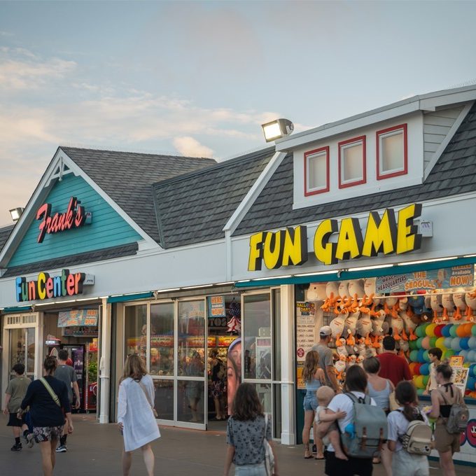 Individuals strolling by a shop with a sign advertising a "fun game".