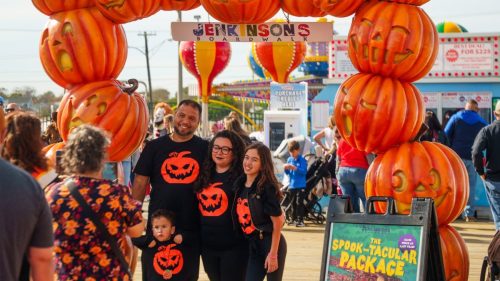 A family wearing matching pumpkin shirts posing for a photo under the pumpkin arch at Jenkinson’s Boardwalk.