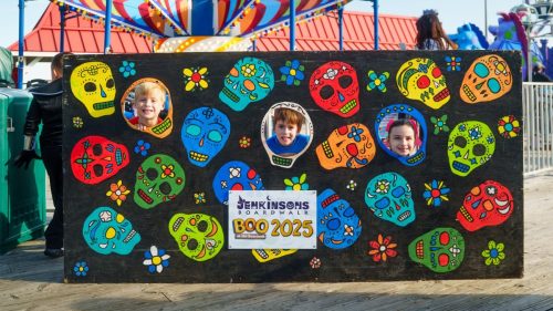 Kids smiling through a colorful sugar skull cutout board at Boo at the Boardwalk 2025.